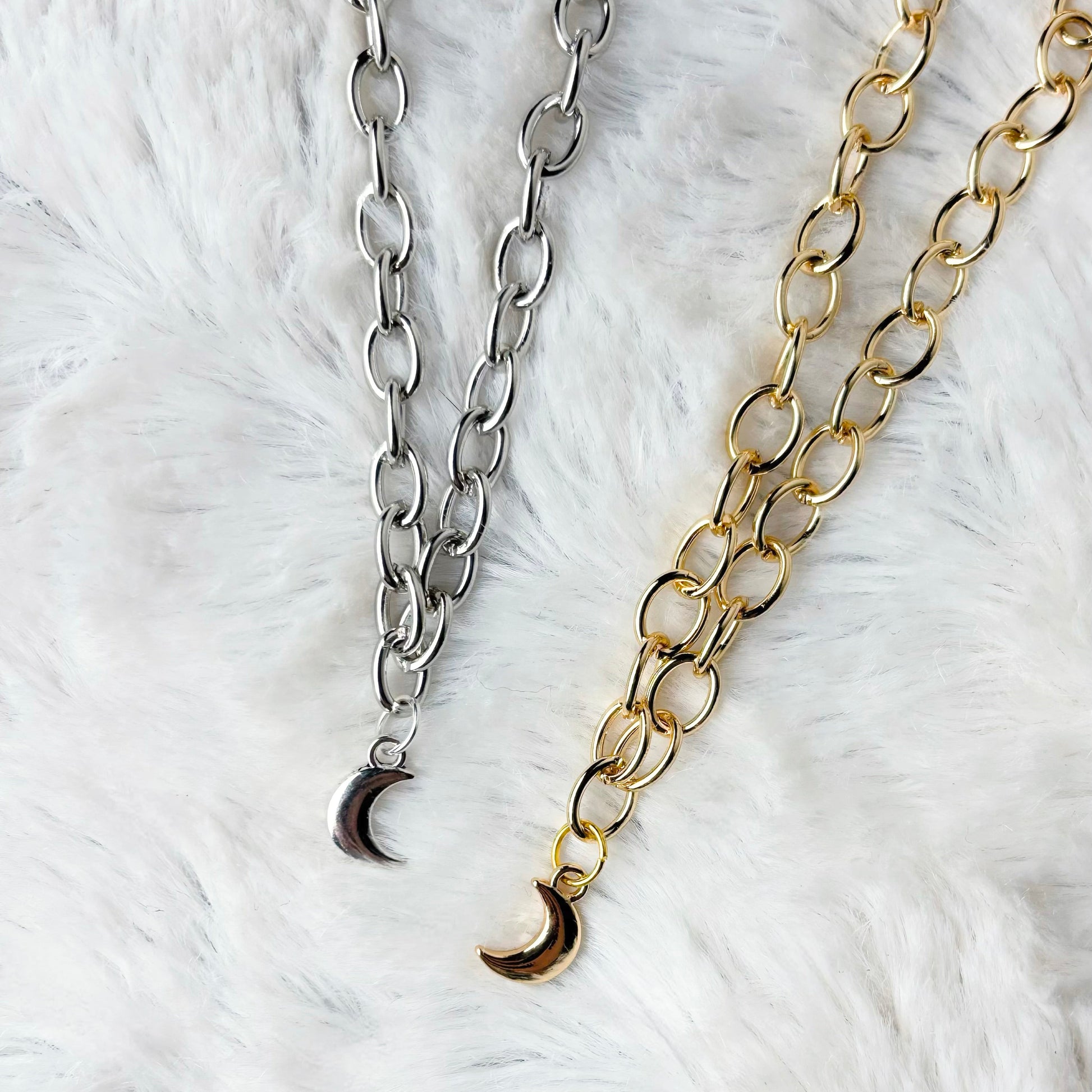 Two chain necklaces with crescent moon pendants on a white fur background
