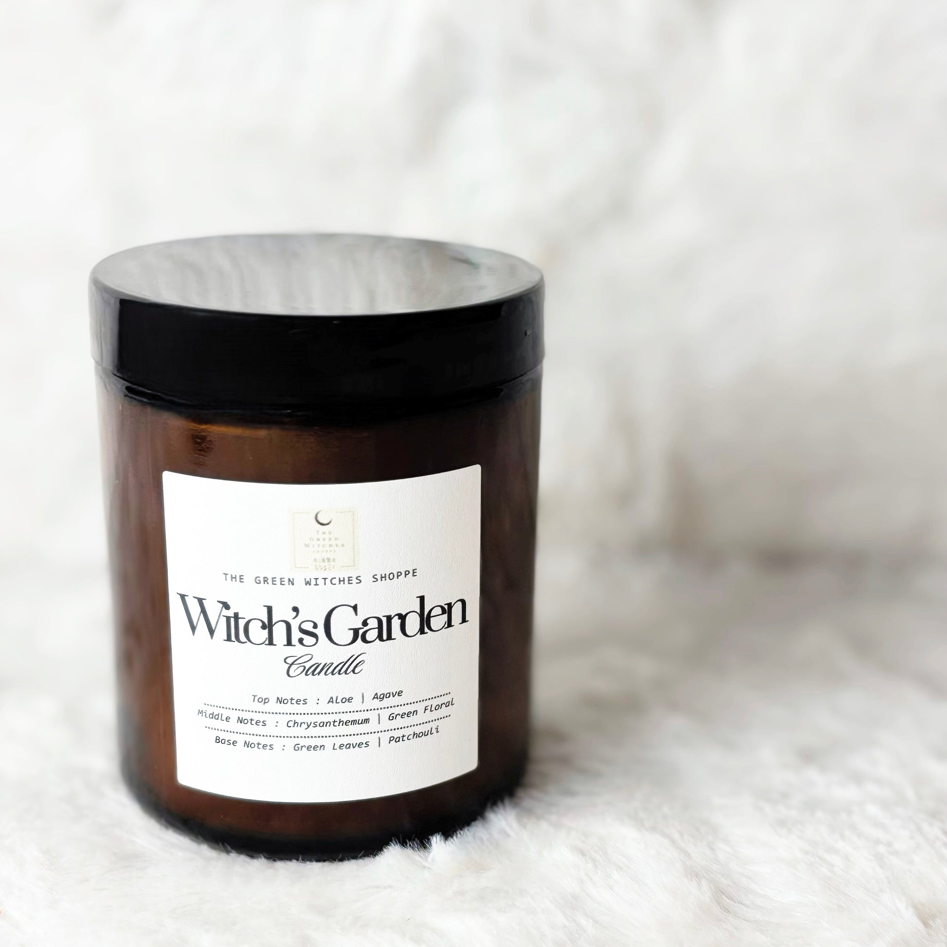 Witch's Garden candle in amber jar with black lid on a white background