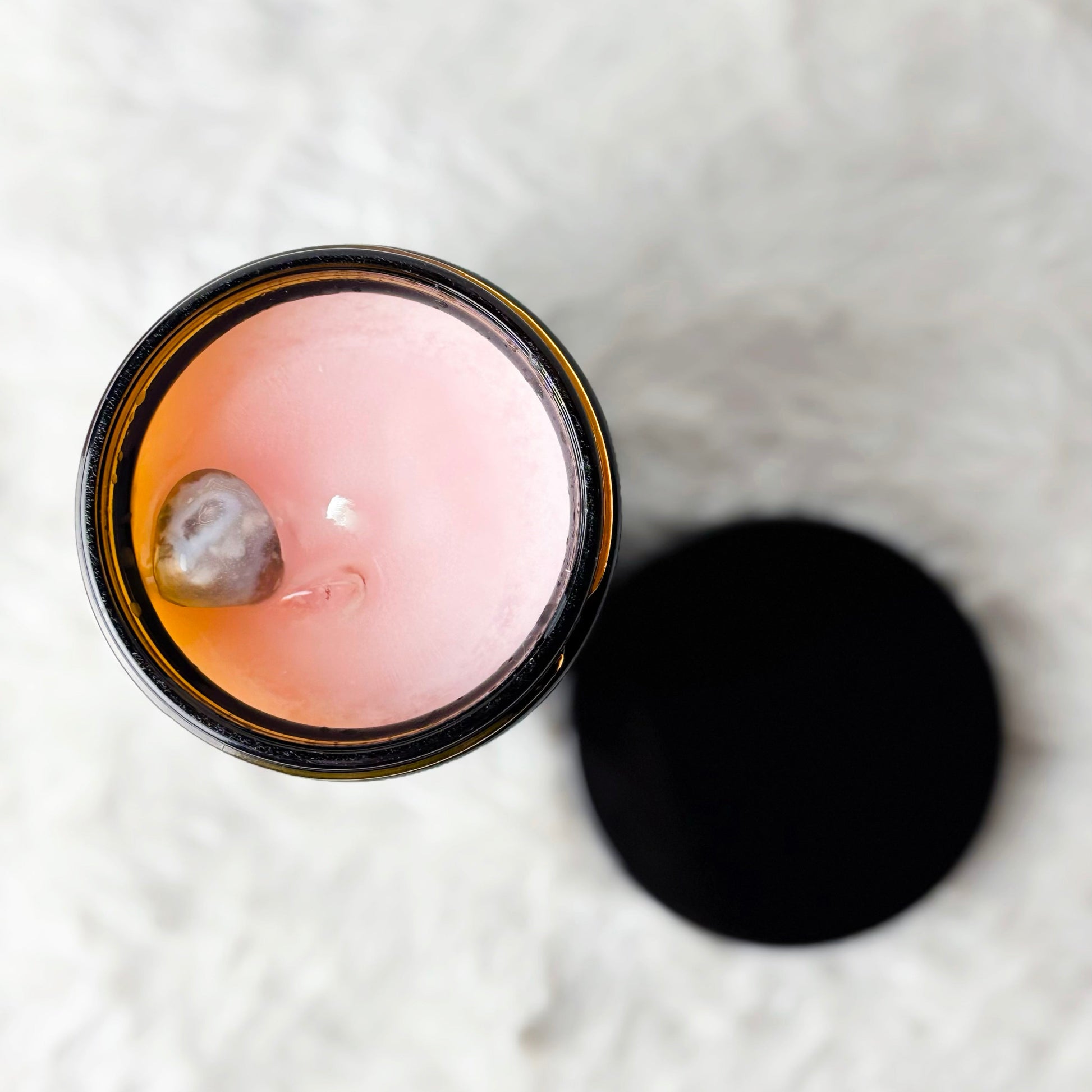 Pink candle in a glass jar with a black lid on a textured white surface