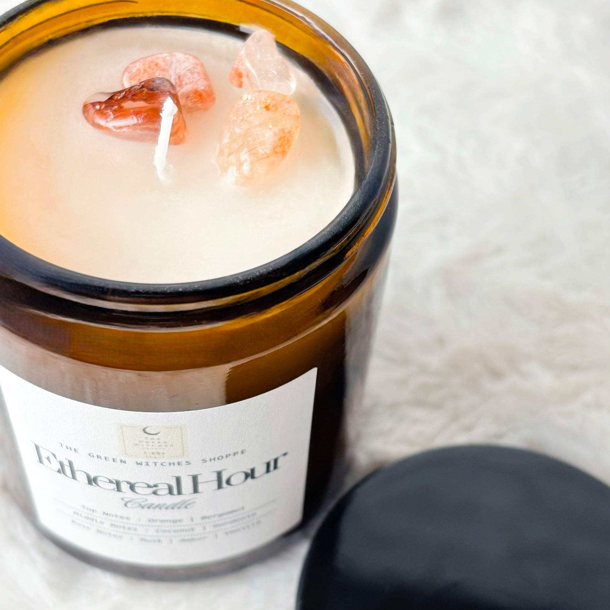 Candle in a glass jar labeled 'Ethereal Hour' on a white textured surface