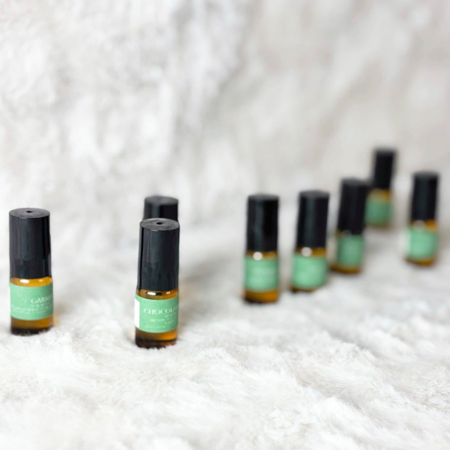 Row of small perfume bottles with green labels on a textured white surface