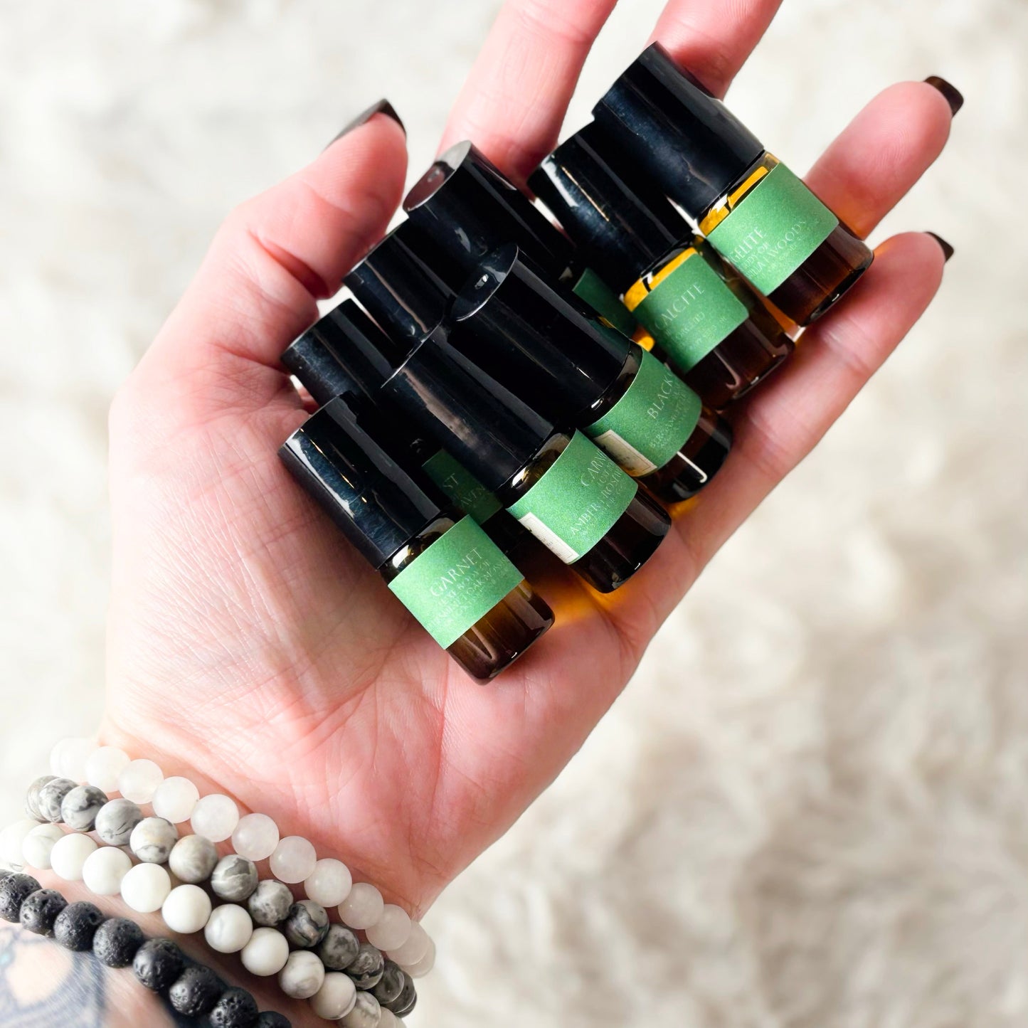Hand holding a set of small black bottles with green caps on a light background
