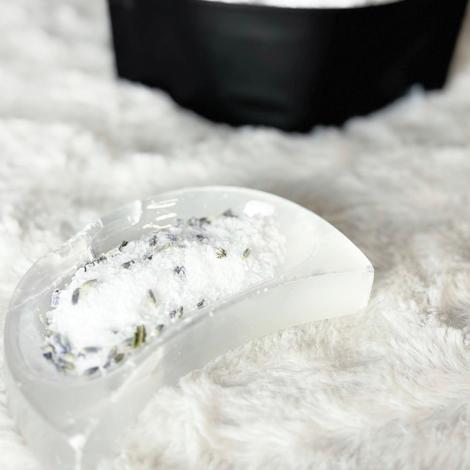 Close-up of a bath soak with green herbs on a fluffy white surface.