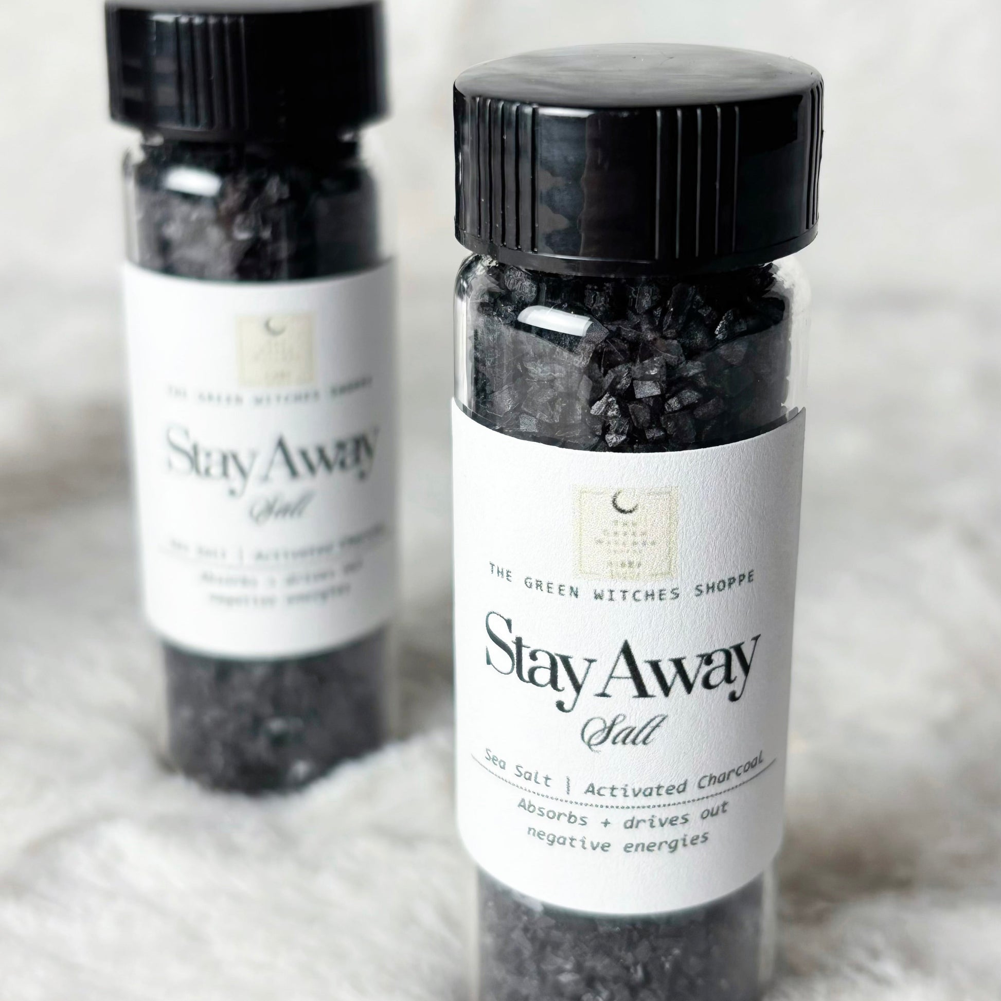Two bottles of 'Stay Away Salt' with black lids on a light gray background