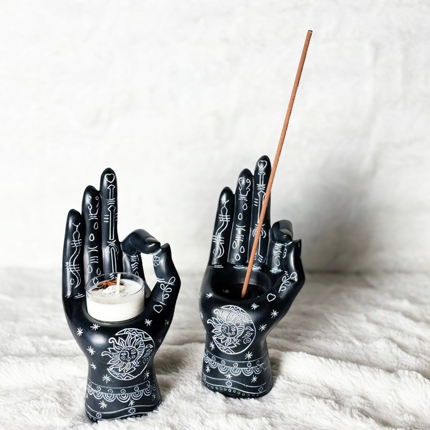 Black hand-shaped candle holders with incense on a white surface