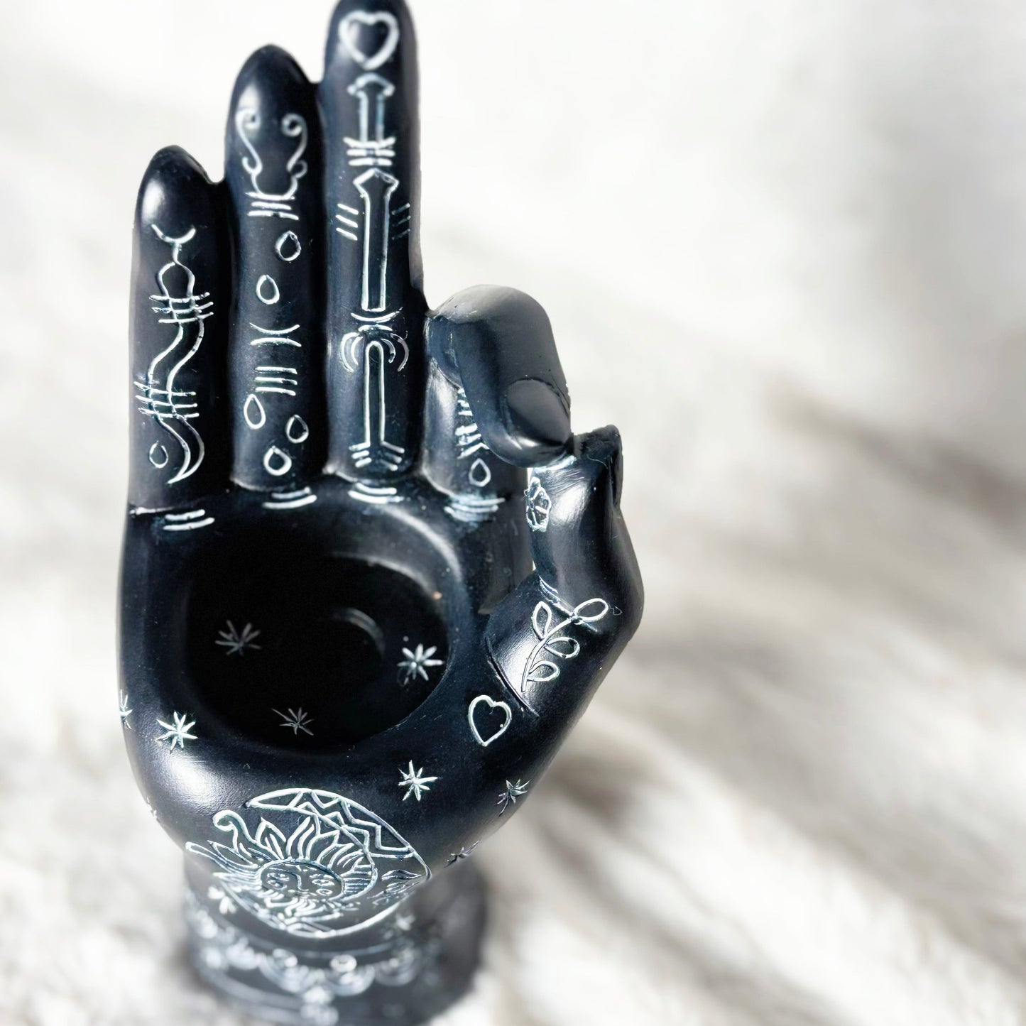 Black hand-shaped ceramic smoking accessory with intricate designs on a white background