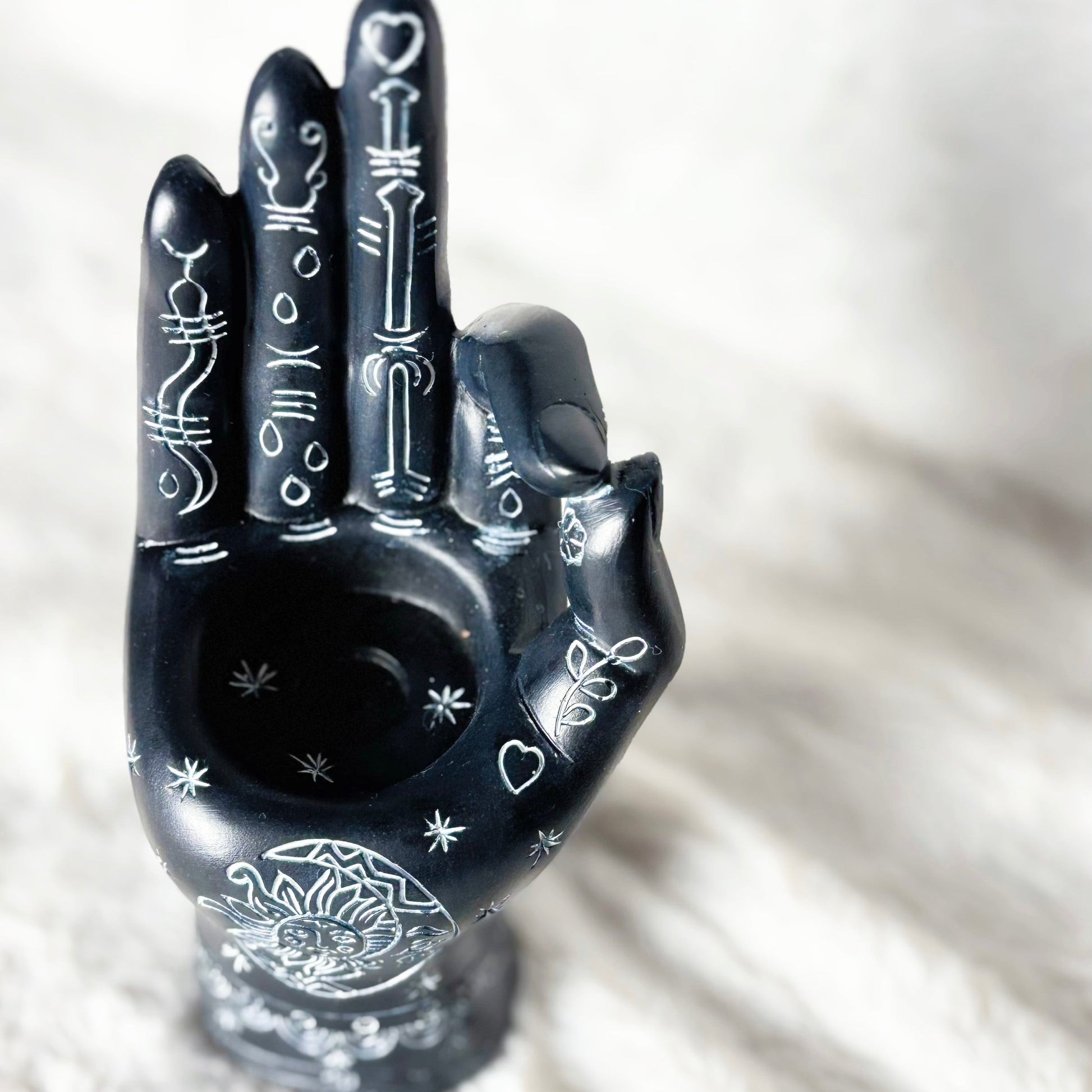 Black hand-shaped ceramic smoking accessory with intricate designs on a white background