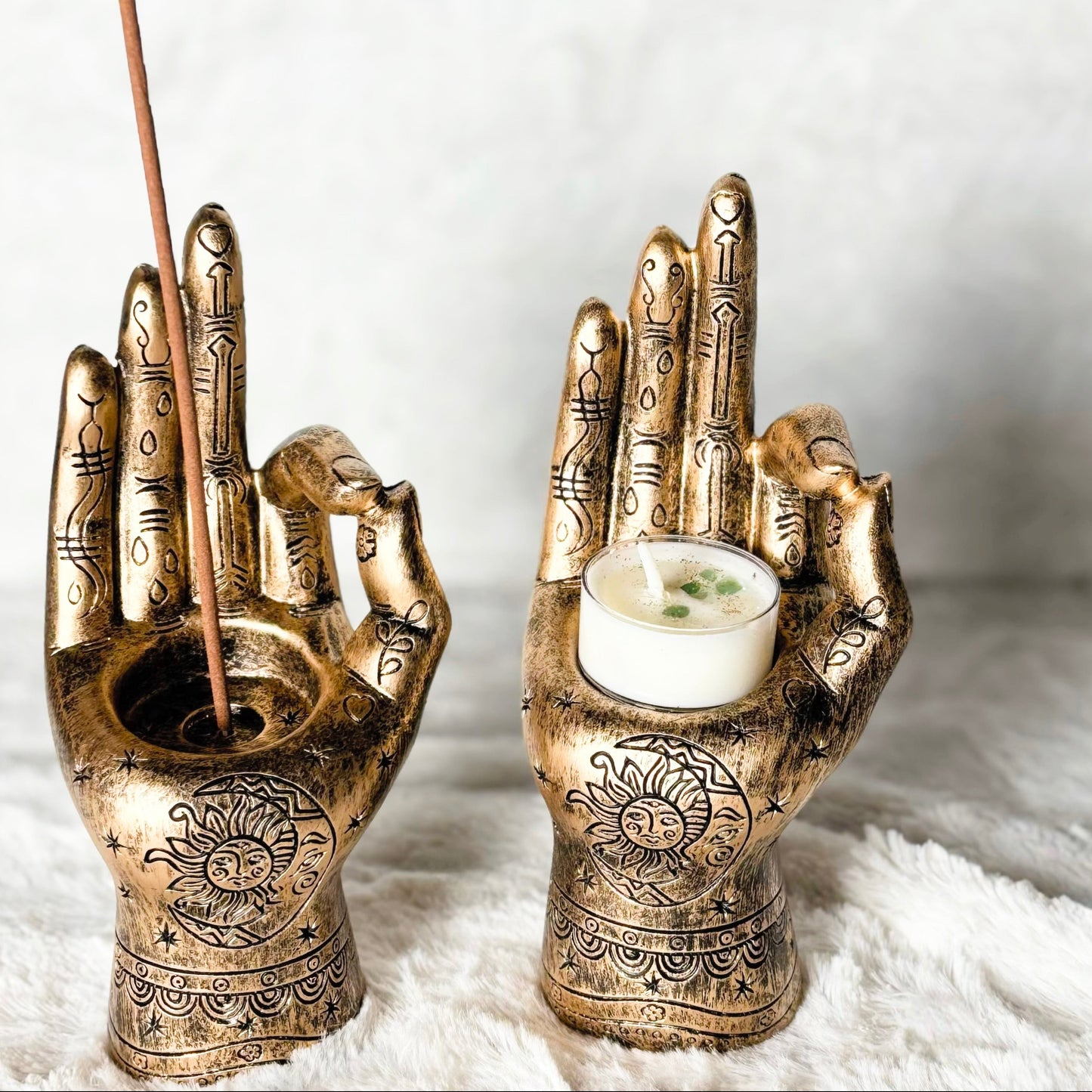 Bronze hand-shaped candle holders with a candle and incense stick on a white background