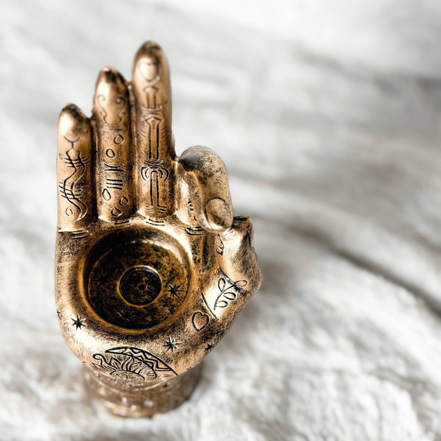 Bronze hand sculpture with intricate designs on a textured white background