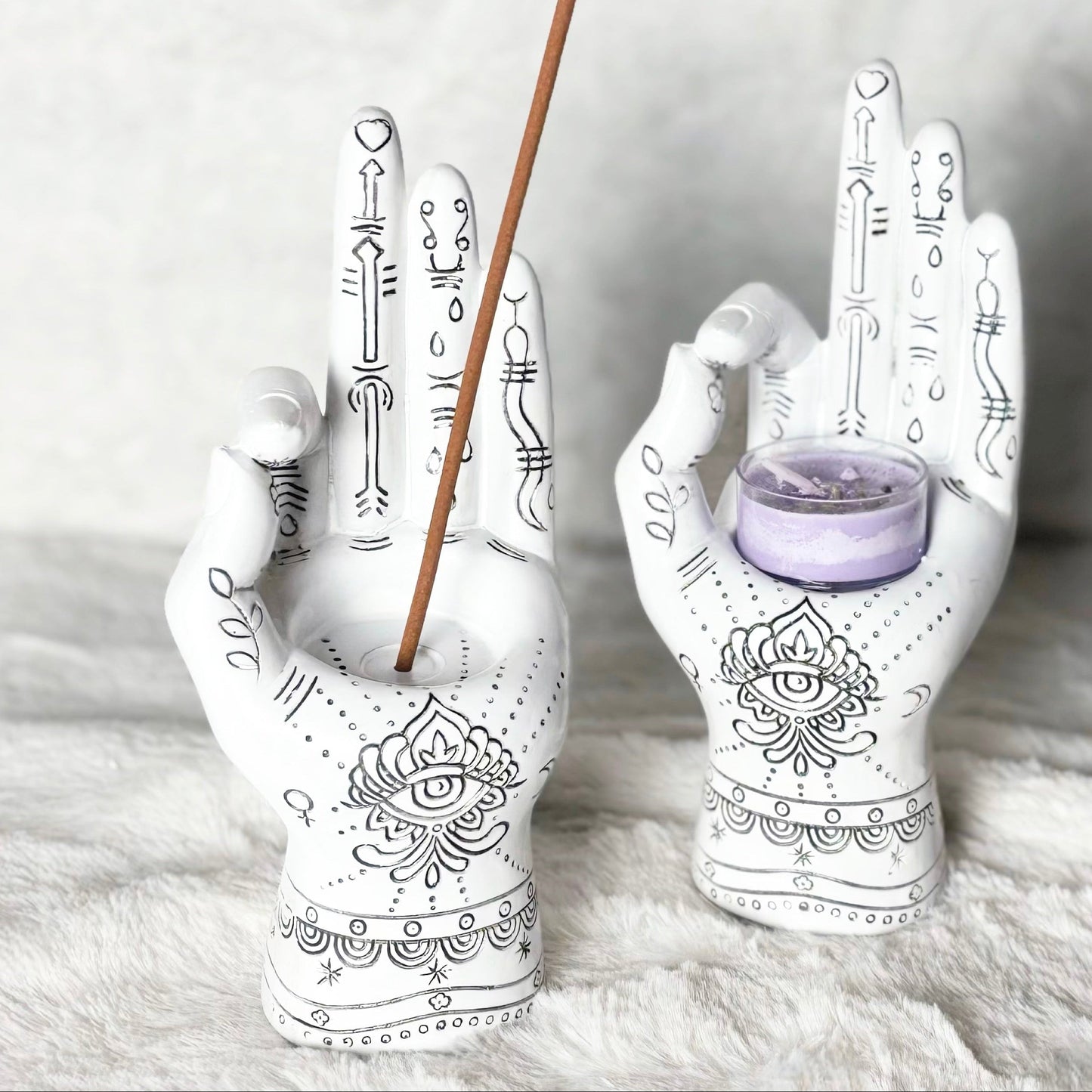 Decorative hand-shaped candle holders with incense stick and small candle on a textured surface.