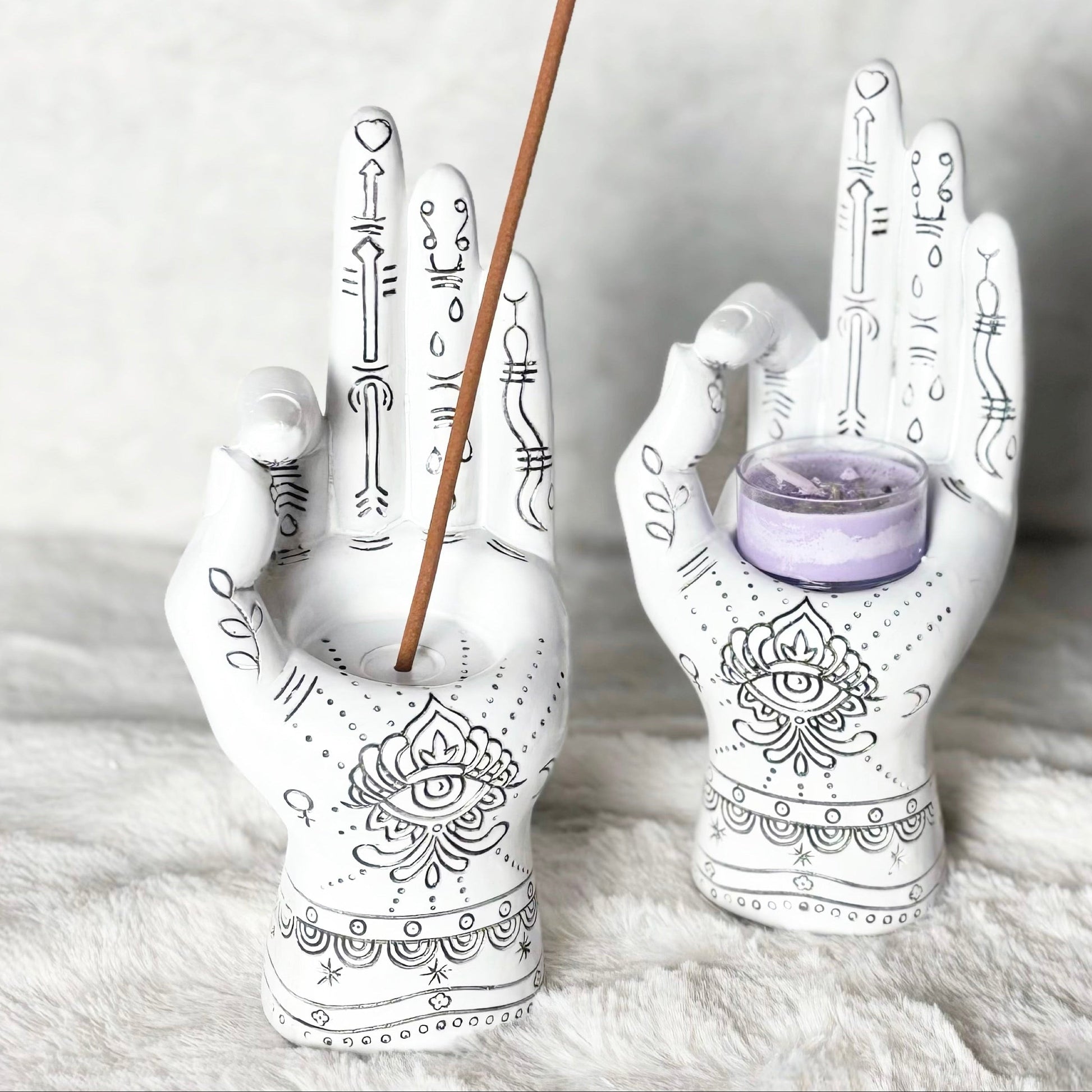 Decorative hand-shaped candle holders with incense stick and small candle on a textured surface.