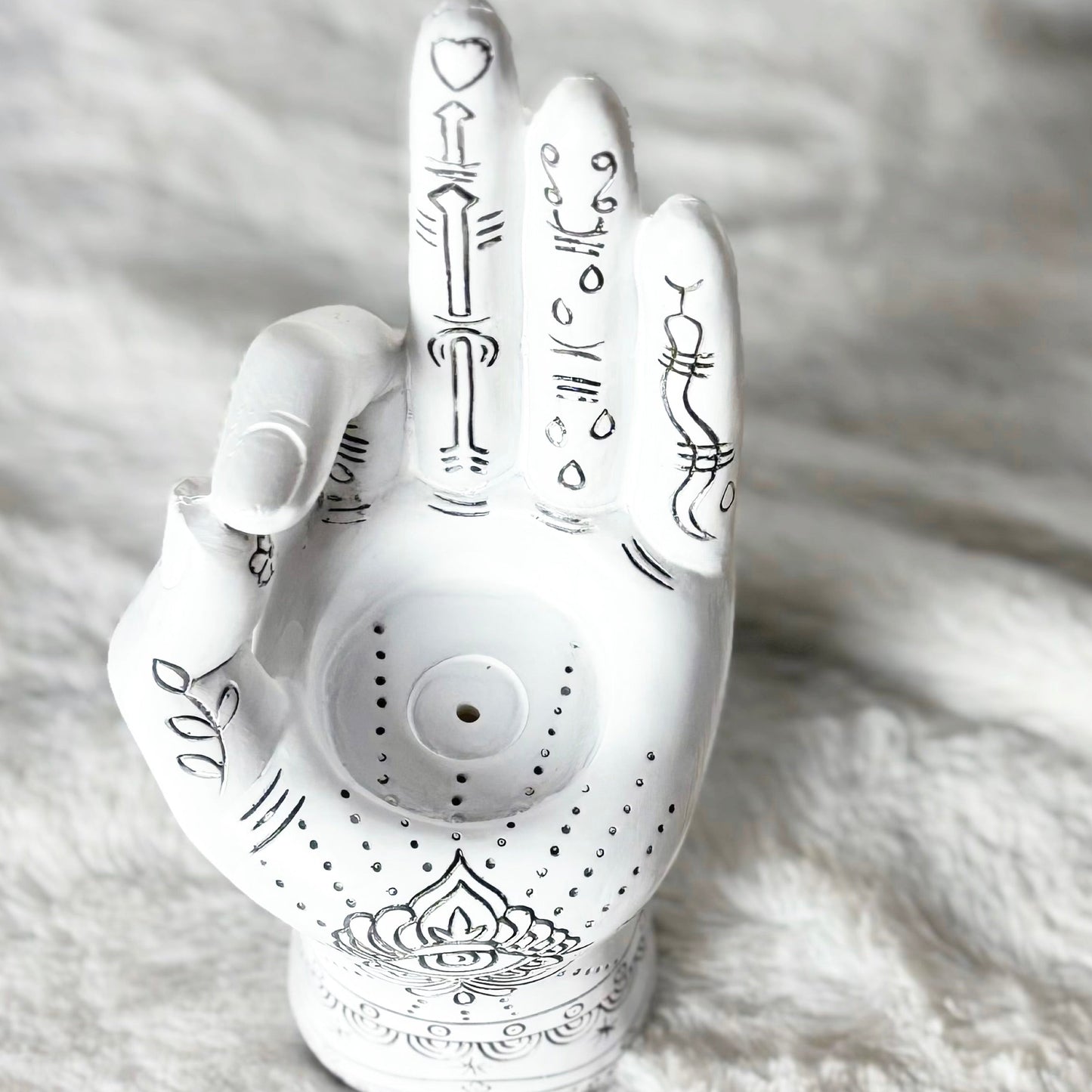 Decorative white hand-shaped object with black designs on a textured white surface