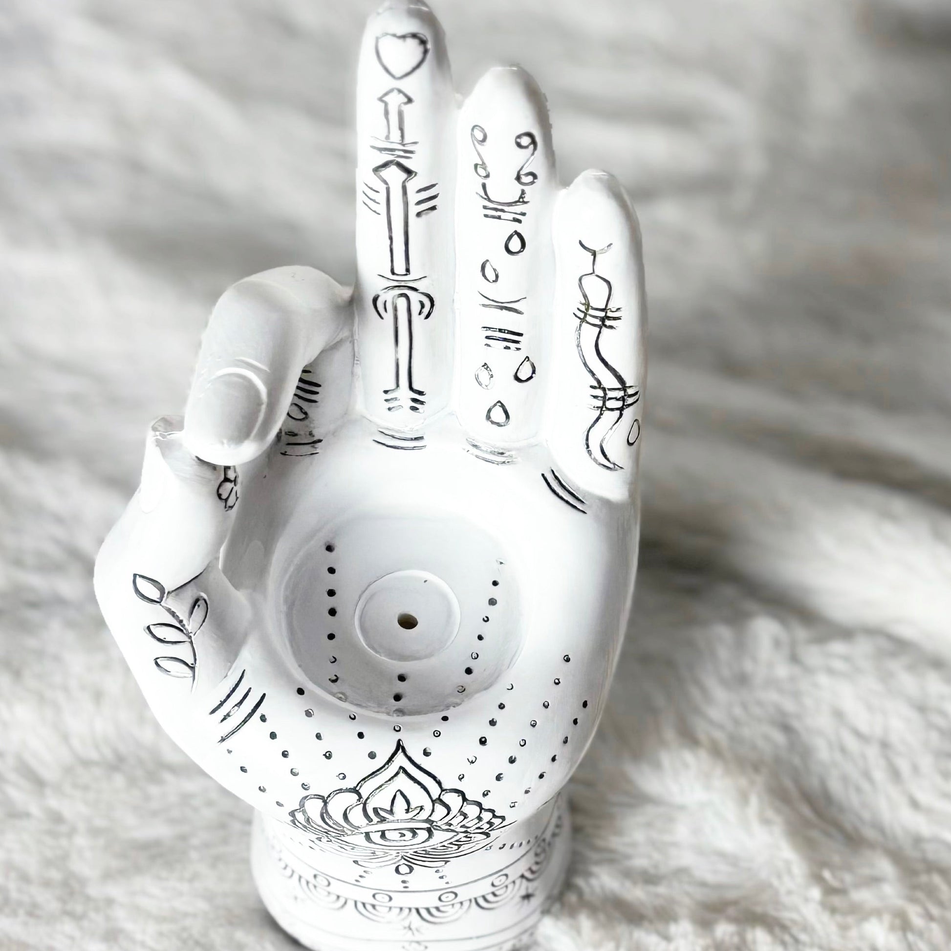 Decorative white hand-shaped object with black designs on a textured white surface