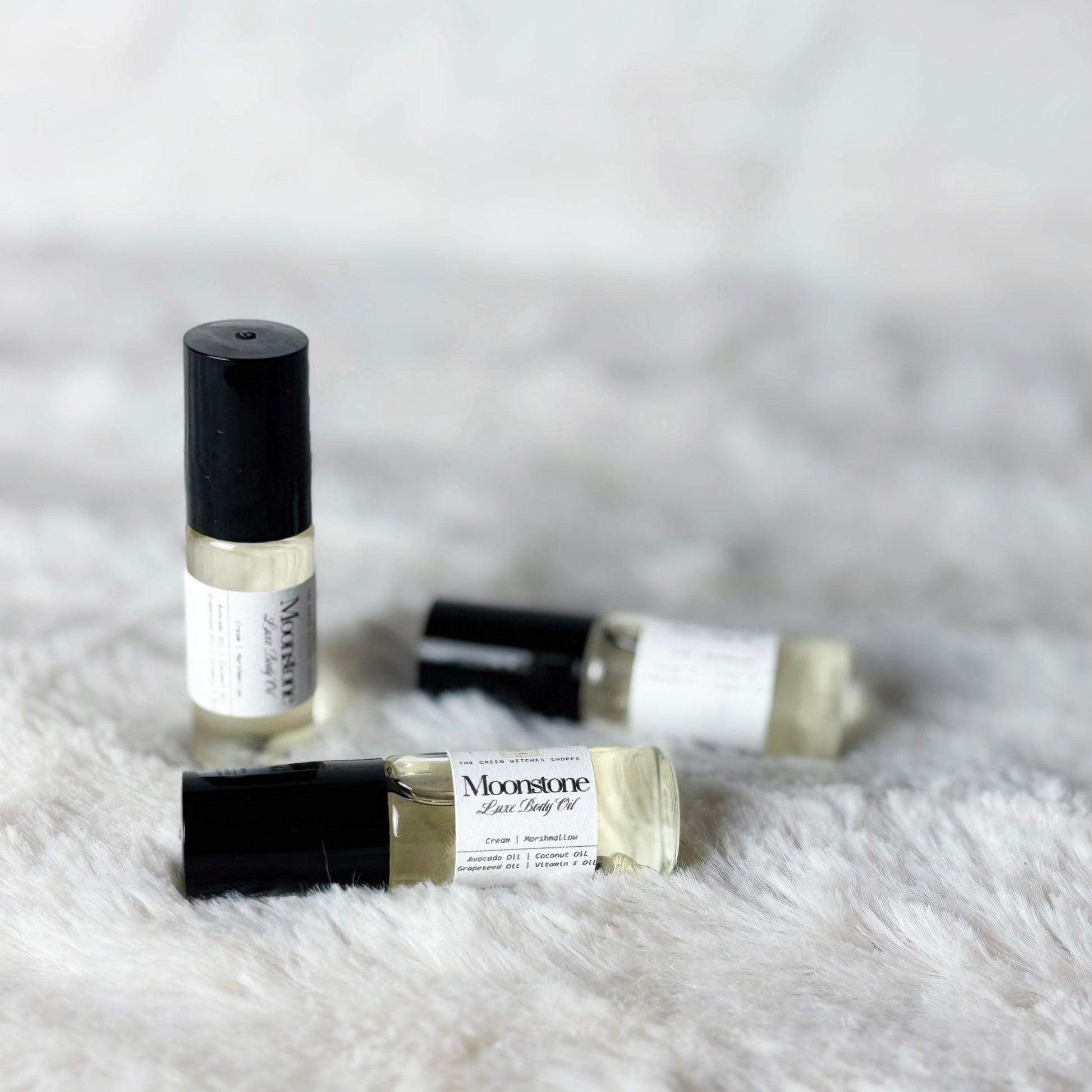 Three small glass bottles with black caps on a white fluffy surface