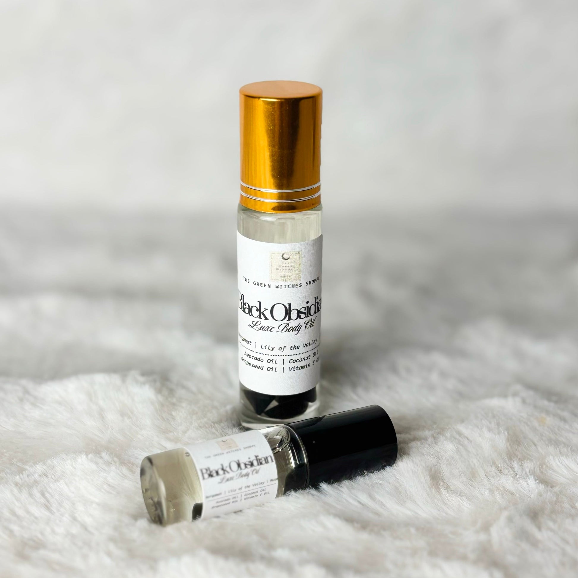 Two small roller bottles of 'Black Orchid' perfume on a white fur surface.