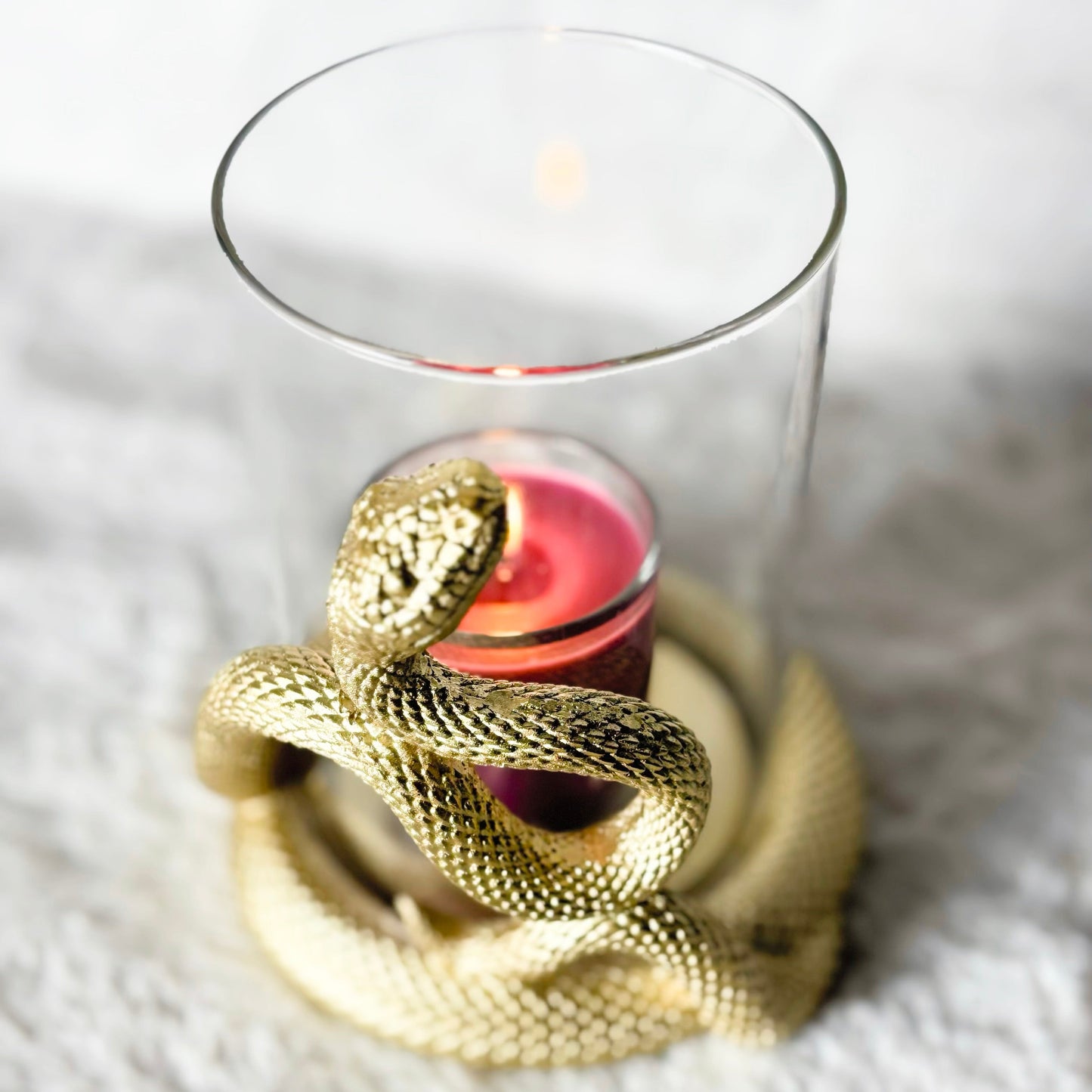 Gold snake-shaped candle holder with a pink candle inside on a white surface