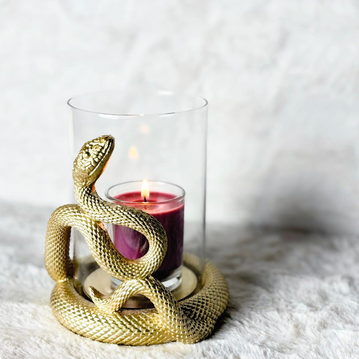 Gold snake-shaped candle holder with a lit candle inside on a white surface.