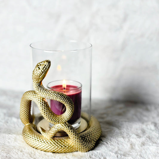 Gold snake-shaped candle holder with a lit candle inside on a white surface.