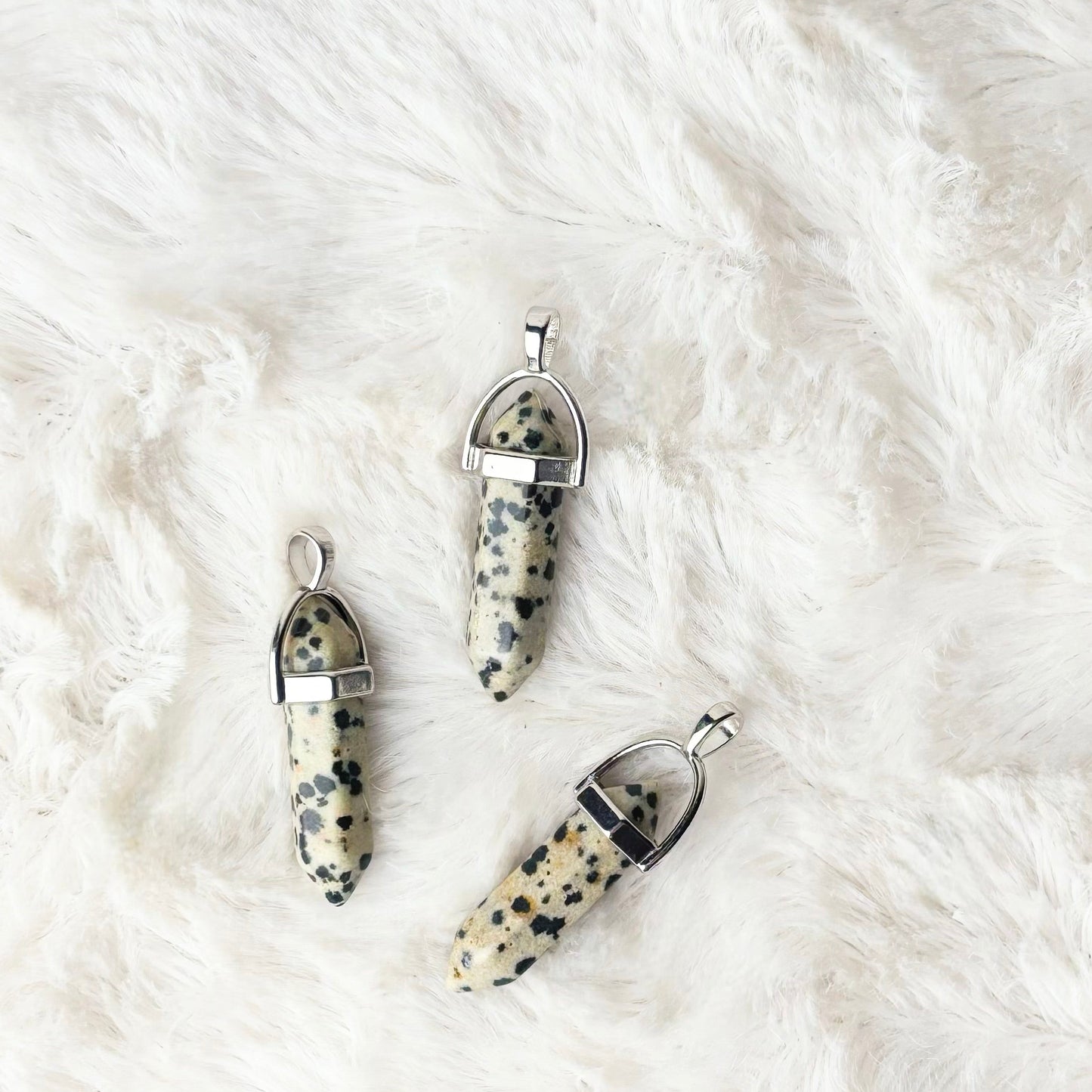 Three dalmatian jasper pendants on a white fur surface