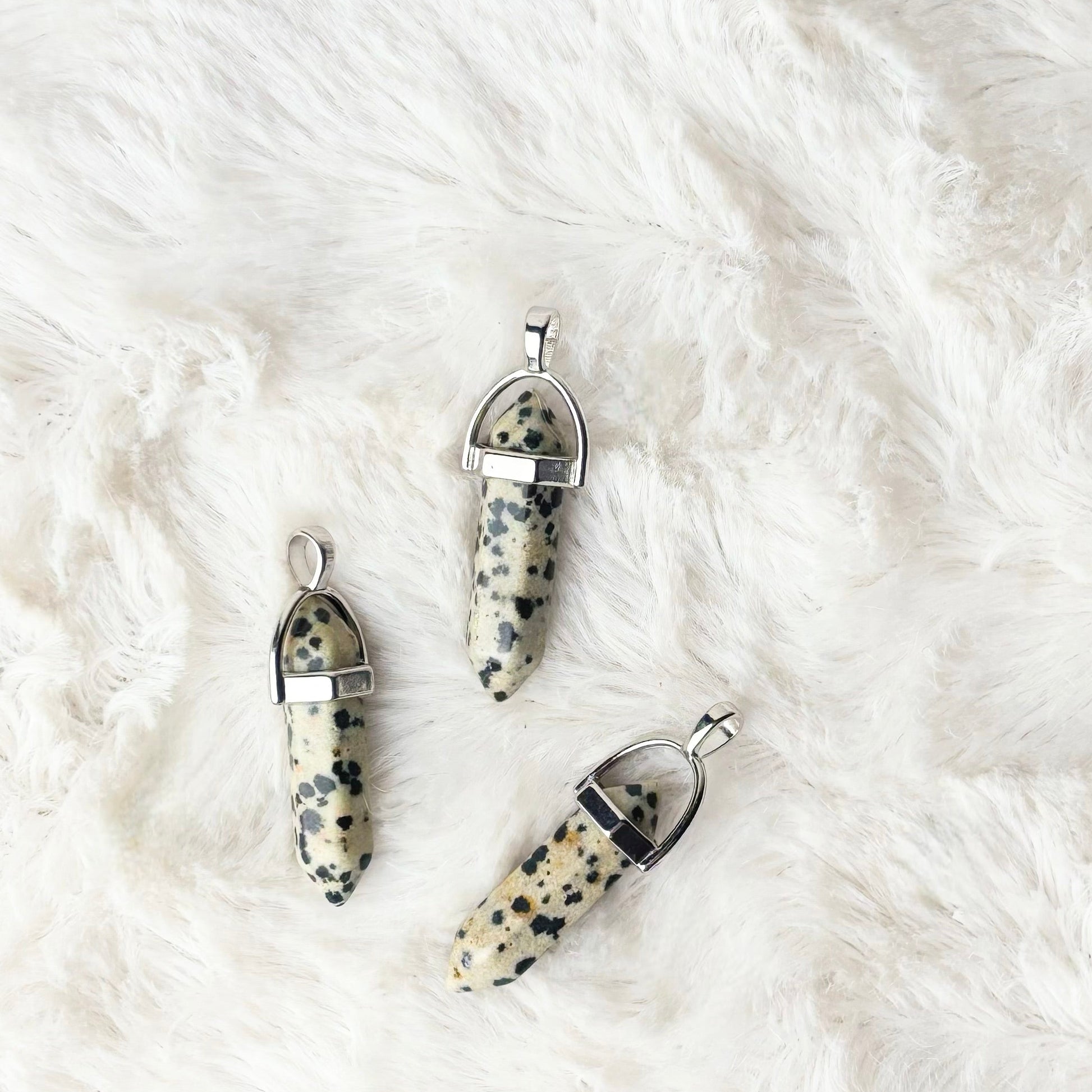 Three dalmatian jasper pendants on a white fur surface