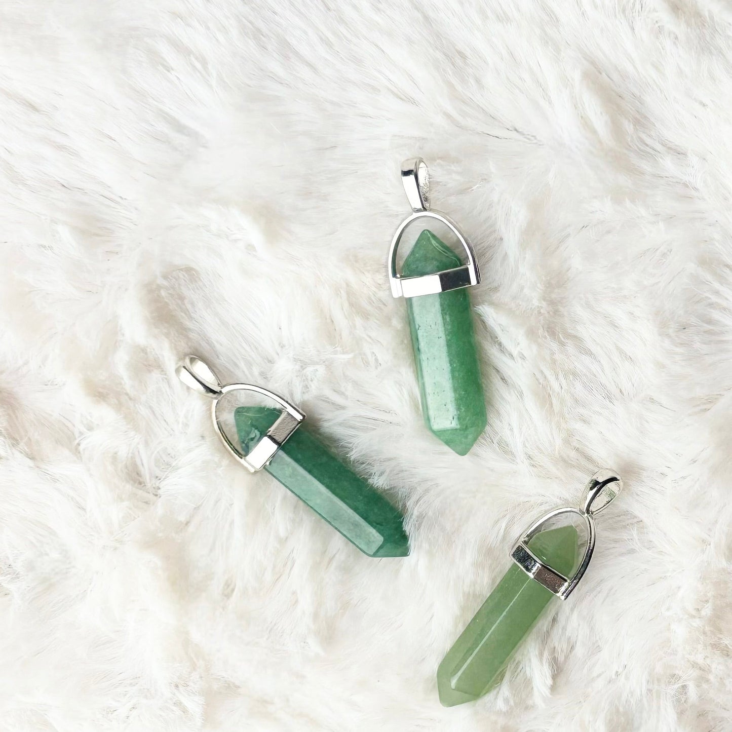 Three green crystal pendants on a white fur surface
