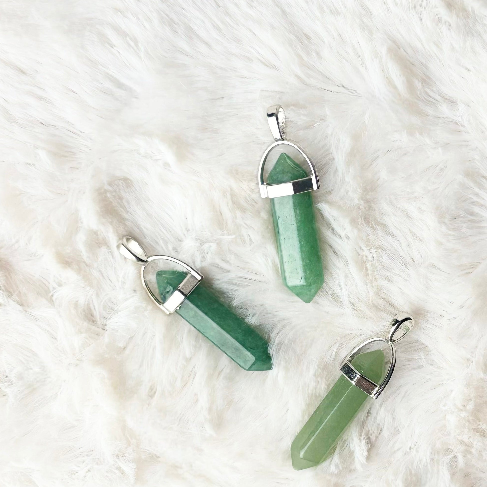 Three green crystal pendants on a white fur surface