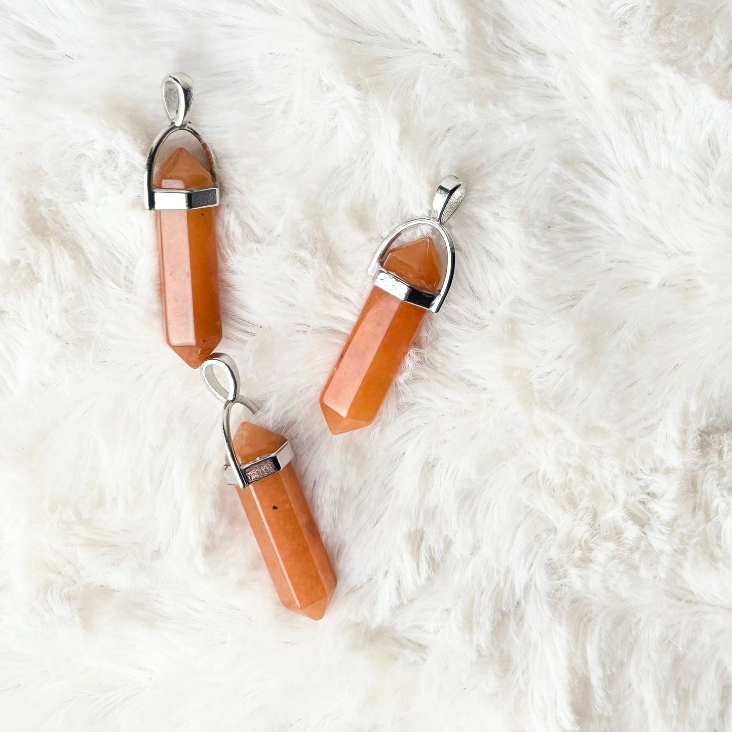 Pair of peach-colored pendant necklaces on a white fur surface