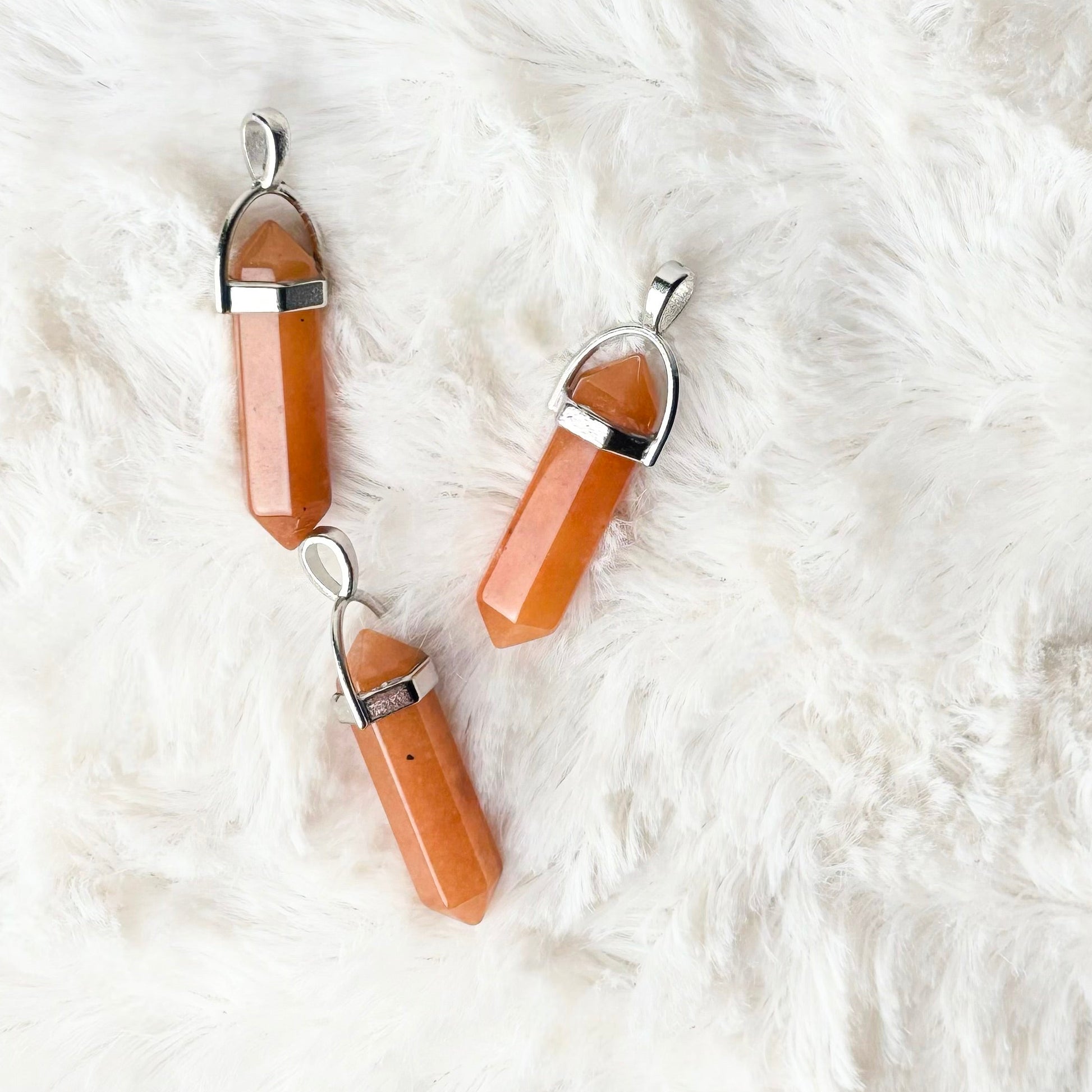 Pair of peach-colored pendant necklaces on a white fur surface