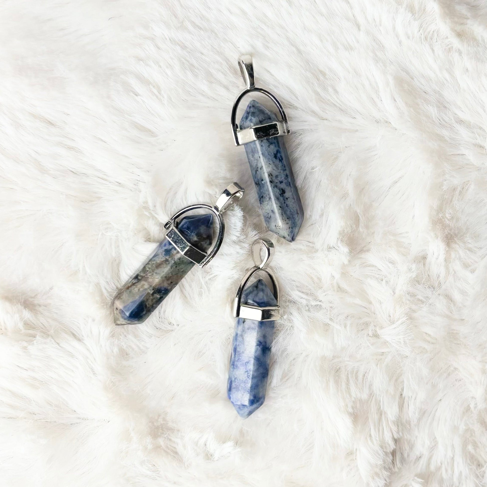 Three blue crystal pendants on a white fur surface
