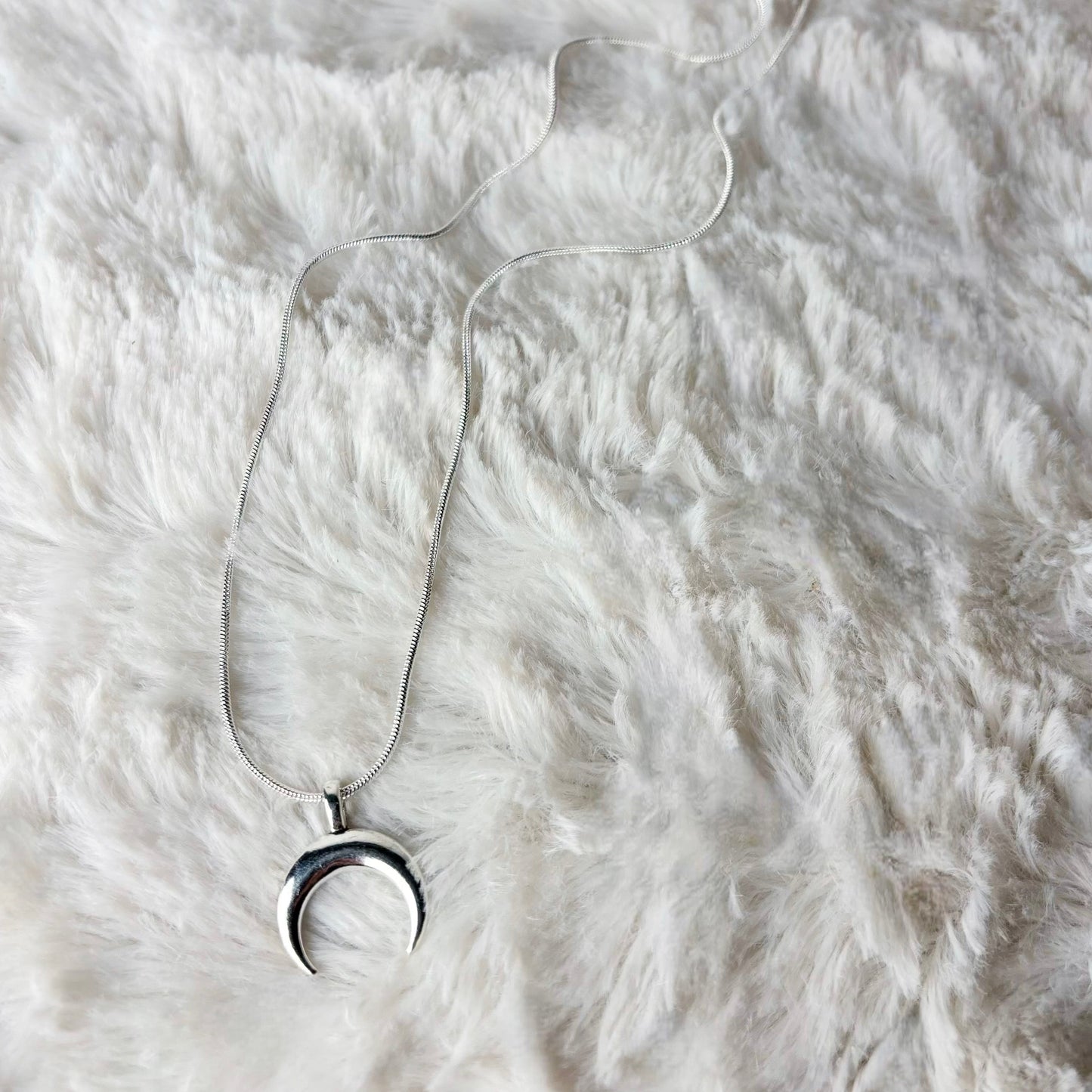 Silver necklace with a crescent moon pendant on a white fur surface