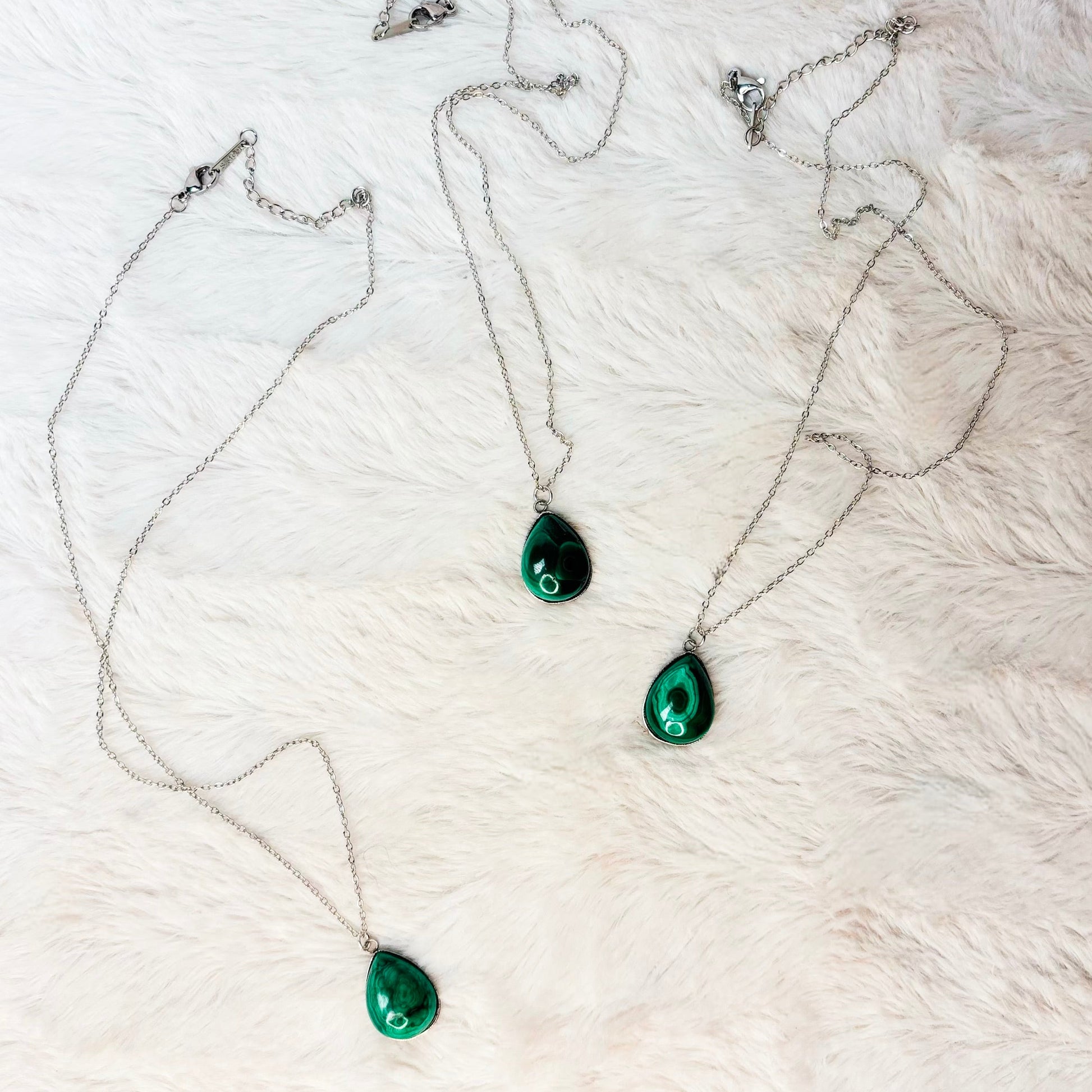 Two green teardrop pendants on silver chains against a white fur background