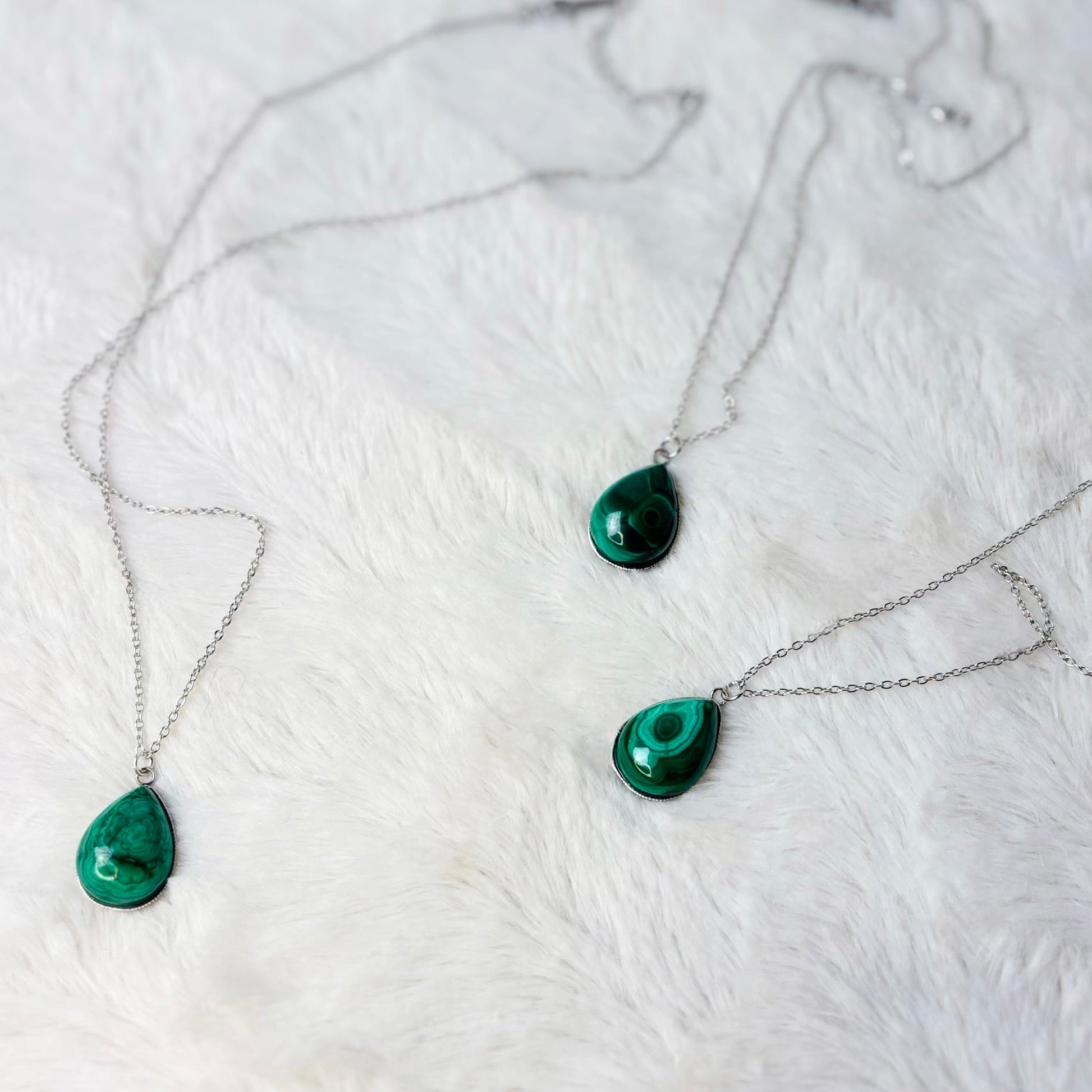 Necklace with green teardrop pendants on a white fur surface