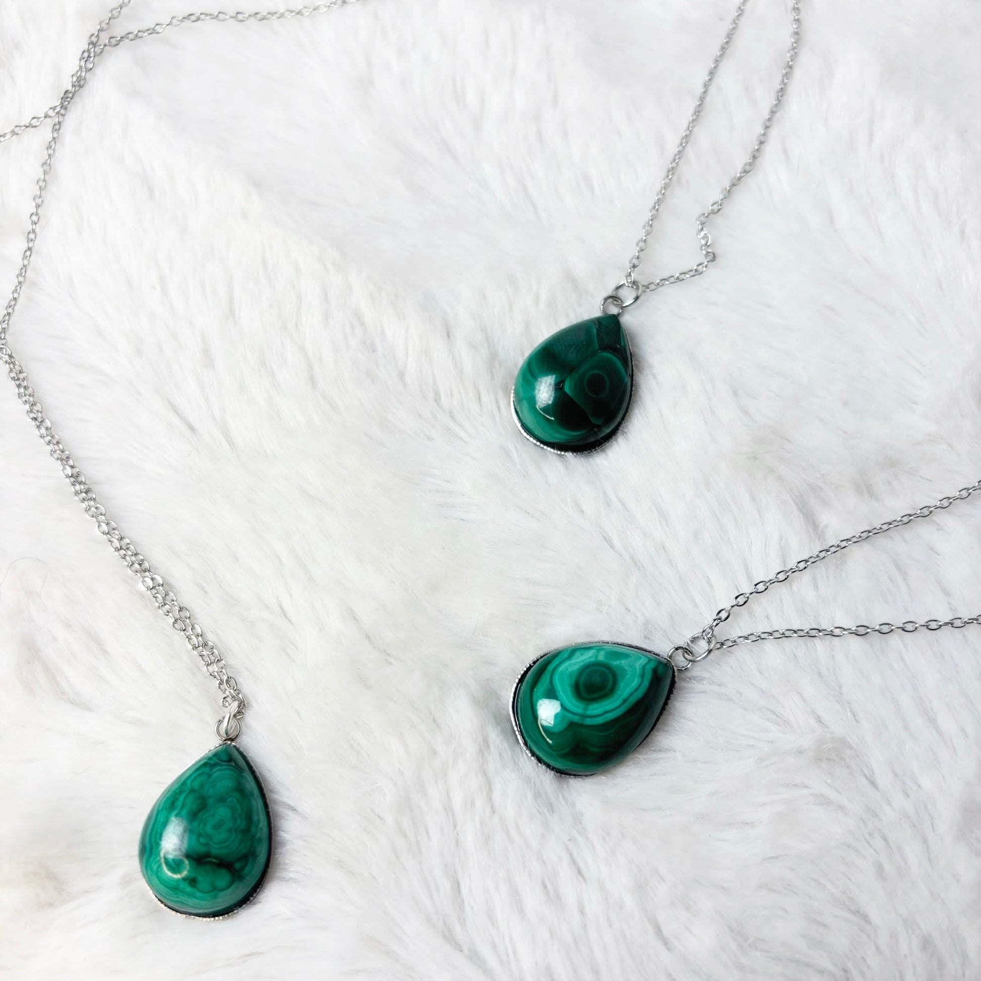 Three green teardrop pendants on silver chains against a white marble background