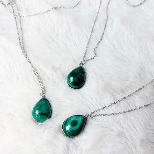 Three green teardrop pendants on silver chains against a white fur background