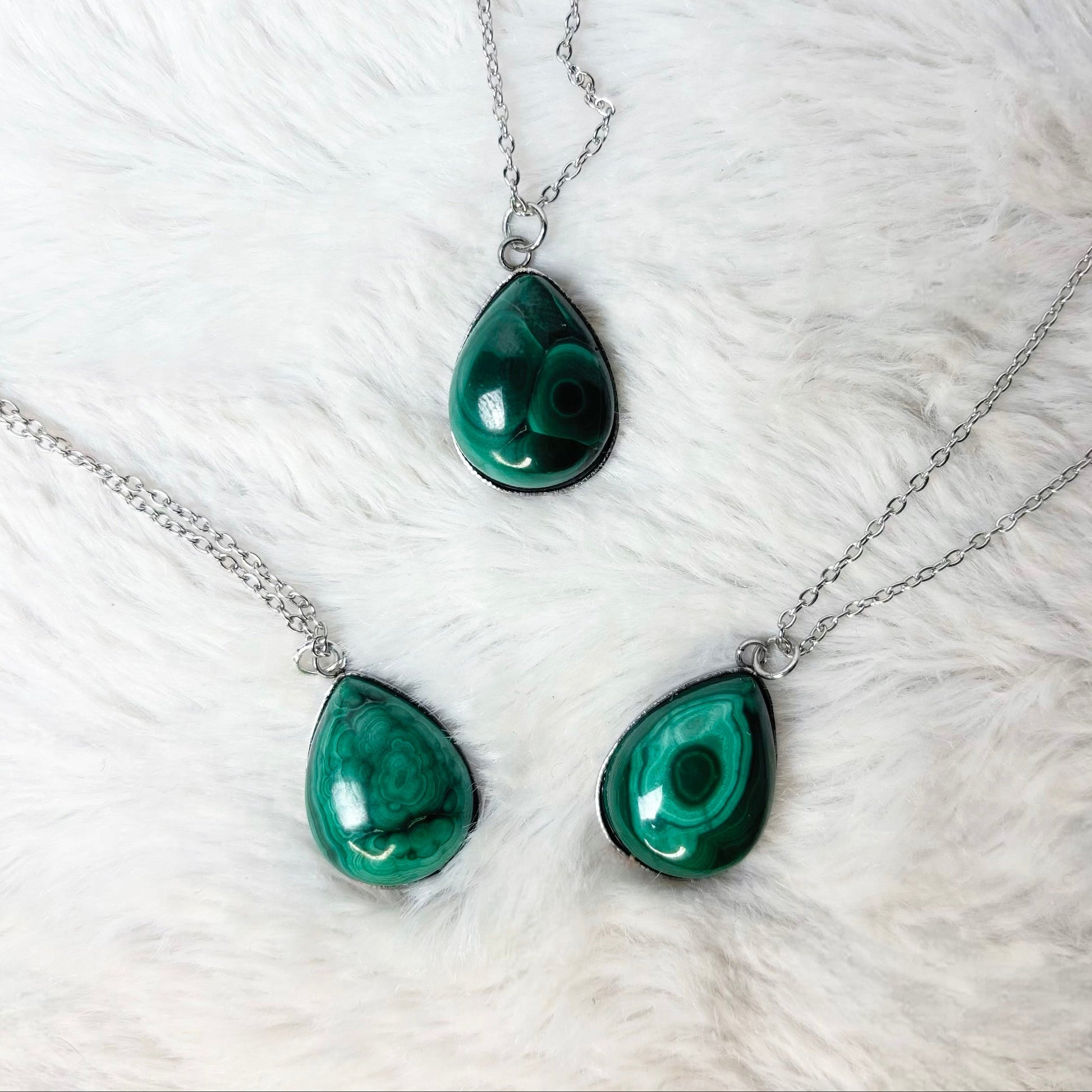 Three green teardrop pendants on silver chains against a white fur background
