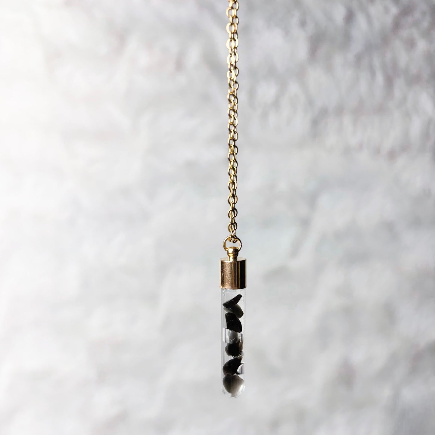 Necklace with a cylindrical pendant on a textured white background