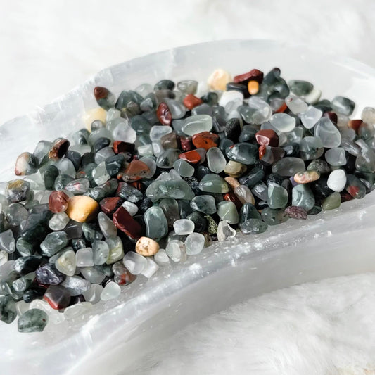 A crescent-shaped clear resin tray filled with small polished multicolored gemstone chips, set on a white faux fur surface.