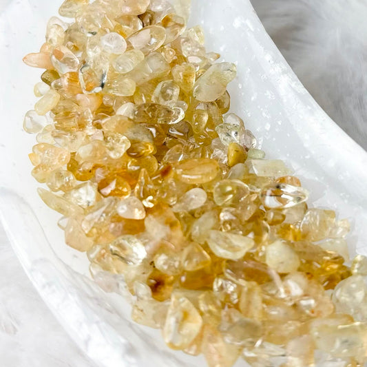 A cluster of small, translucent golden-yellow crystals arranged in a white crescent-shaped dish on a soft white faux fur surface.