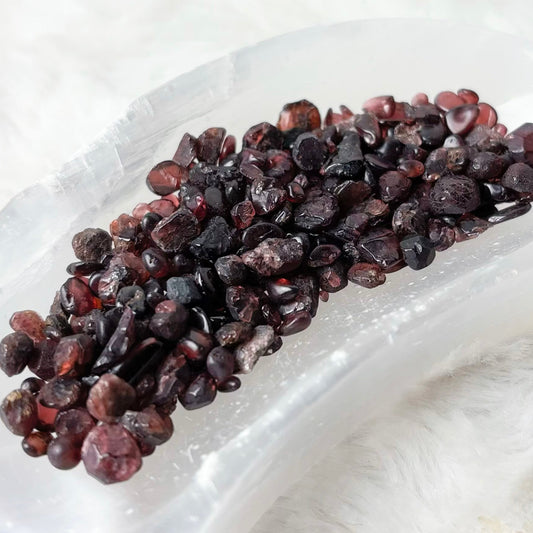 A curved, translucent white resin tray holding a small pile of dark brown dried berries, set against a soft white faux fur background.