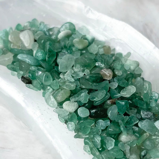 Green raw crystal chips arranged in a white crescent-shaped dish on a soft white faux fur background.
