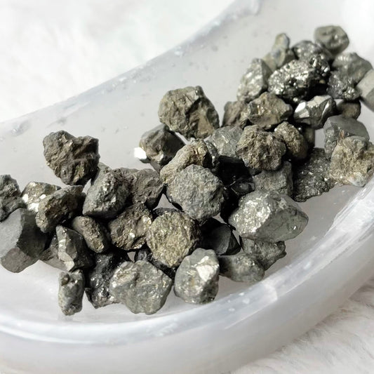 Raw metallic pyrite crystals in a small white dish on a white faux fur background.