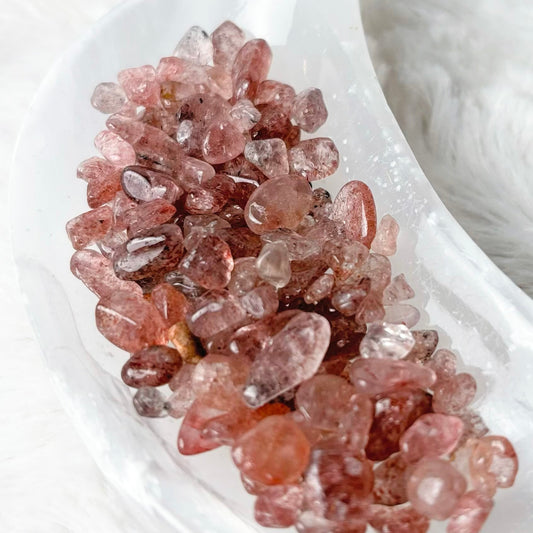 A cluster of raw rose quartz crystal chips in a white crescent-shaped dish, set against a soft white faux fur background.