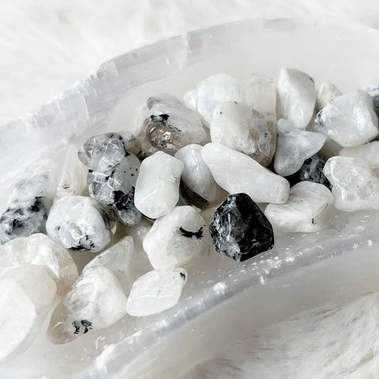 A crescent-shaped clear resin tray filled with smooth white, gray, and black tumbled stones, placed on a white faux fur surface.