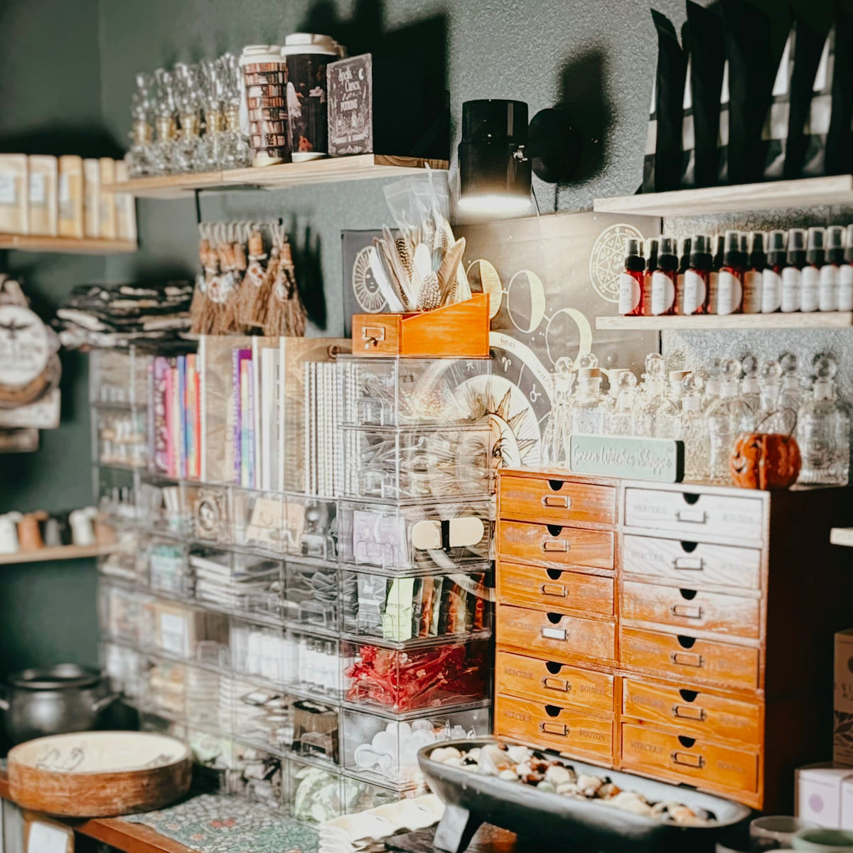 A cozy, dimly lit boutique interior filled with shelves of glass bottles, jars, clear organizer drawers, wooden drawers, and decorative items, with a warm spotlight on the wall.