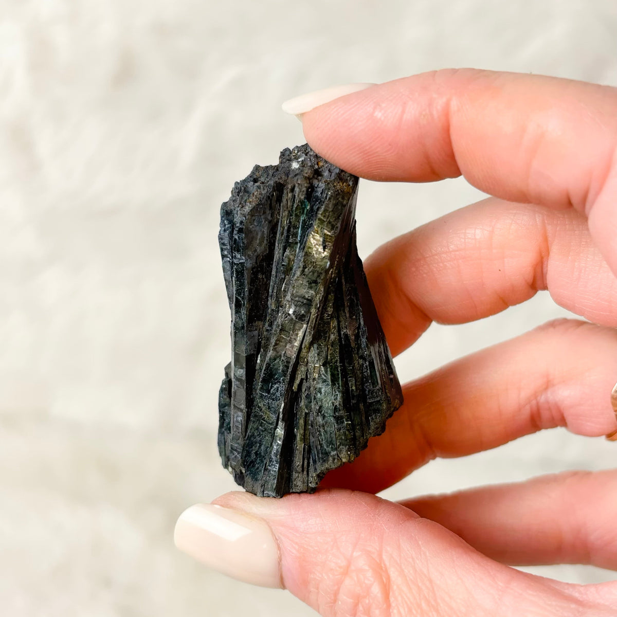 Hand holding a Vivianite specimen on a white background