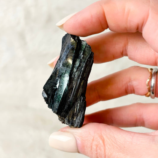 Hand holding a Vivianite specimen on a white background