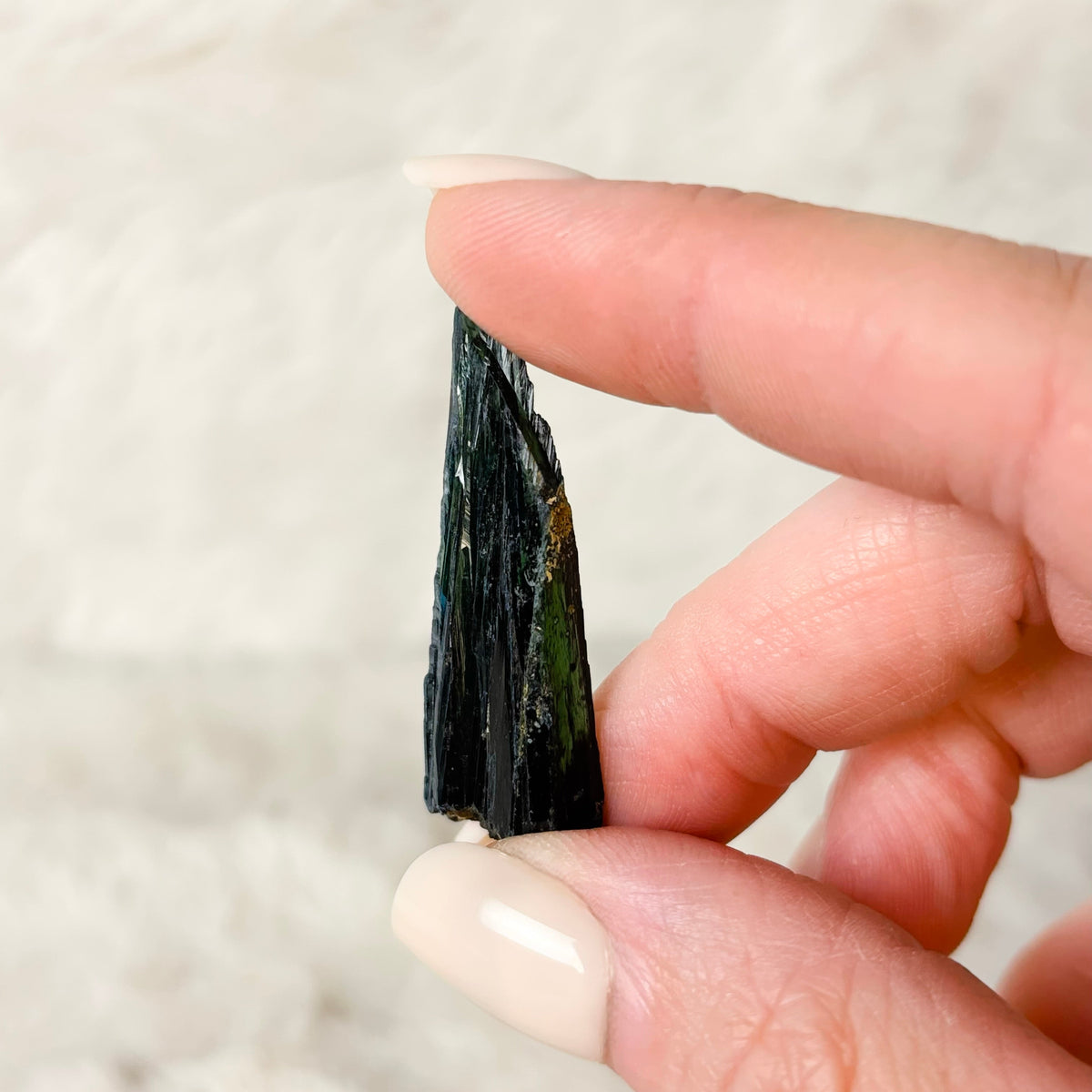Hand holding a Vivianite specimen on a white background