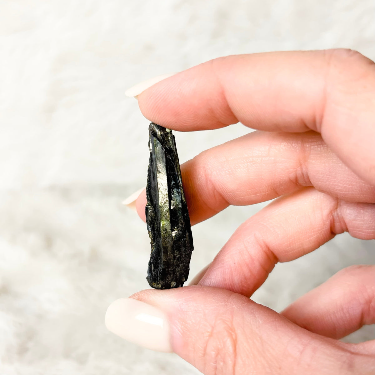 Hand holding a Vivianite specimen on a white background