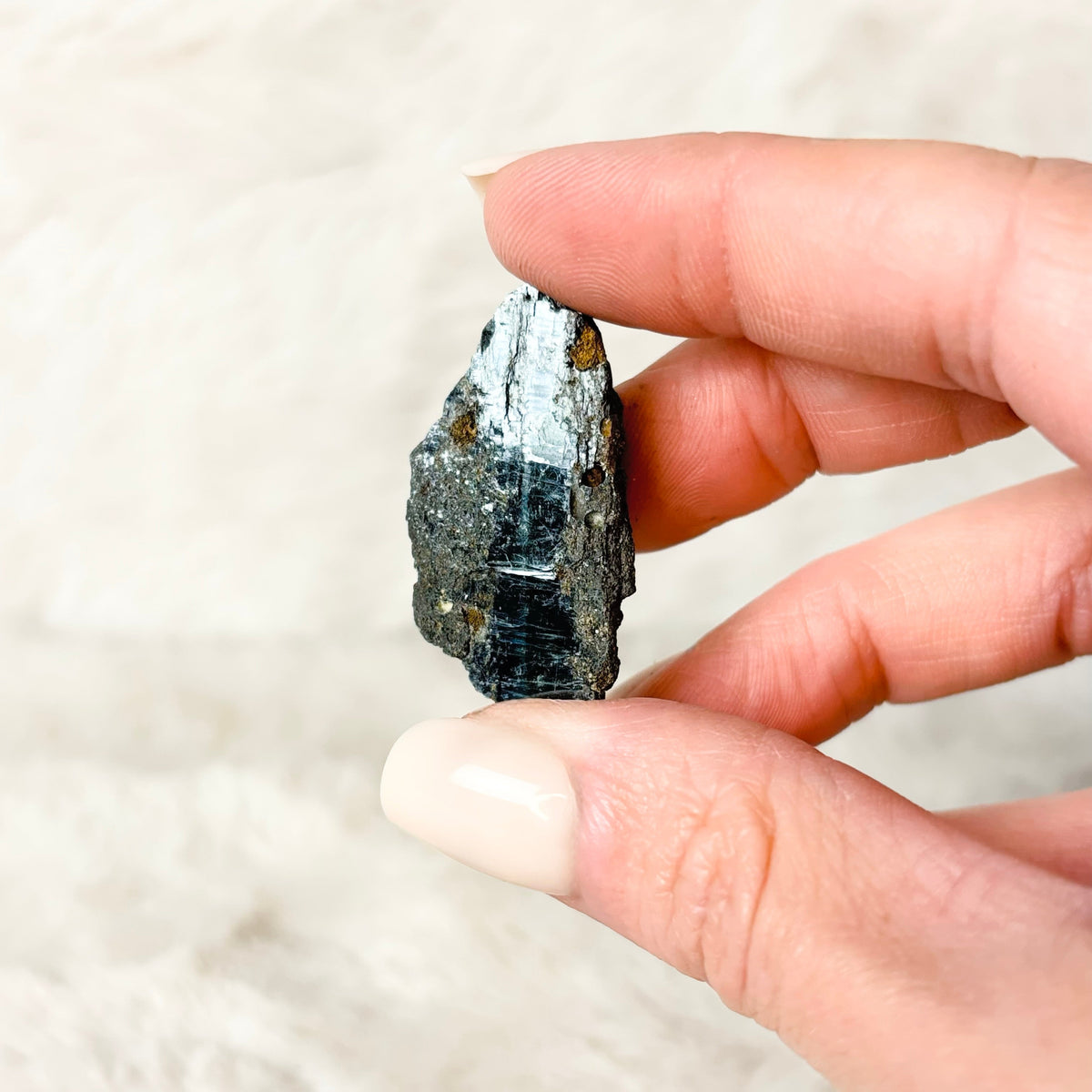 Hand holding a Vivianite specimen on a white background