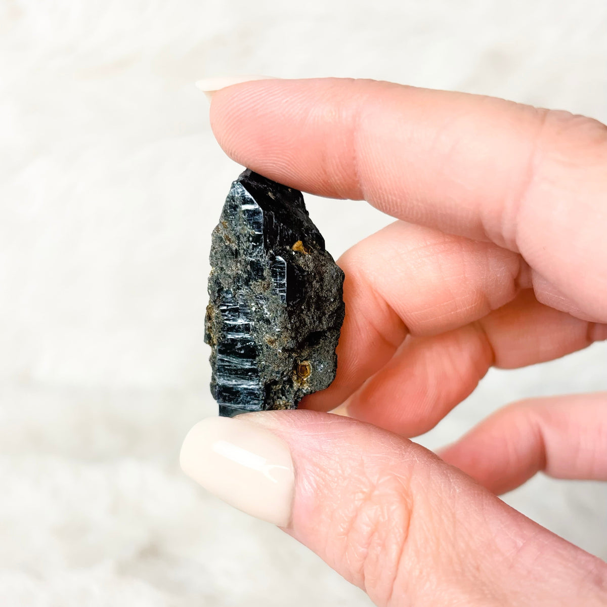 Hand holding a Vivianite specimen on a white background